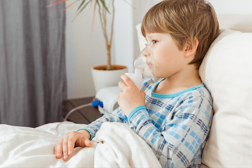 mały chłopiec leżący w łóżku z inhalatorem