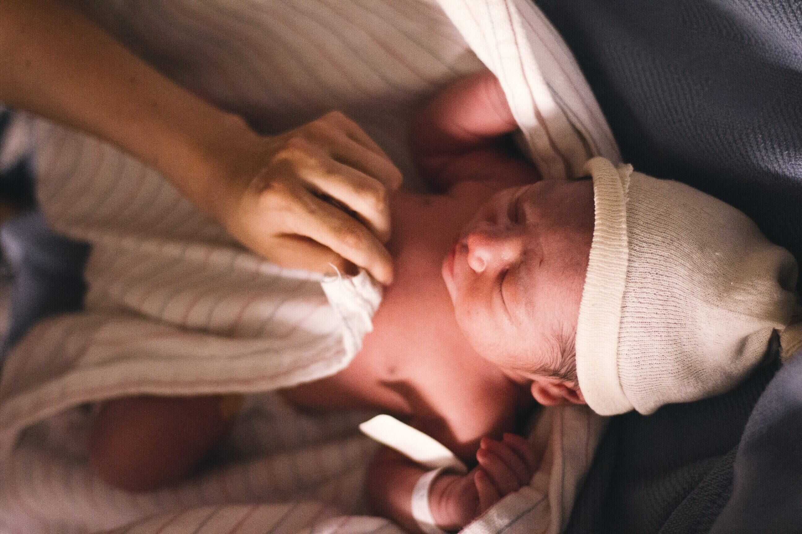 Noworodek w szpitalu z opaską na ręku otulany w pieluszkę.