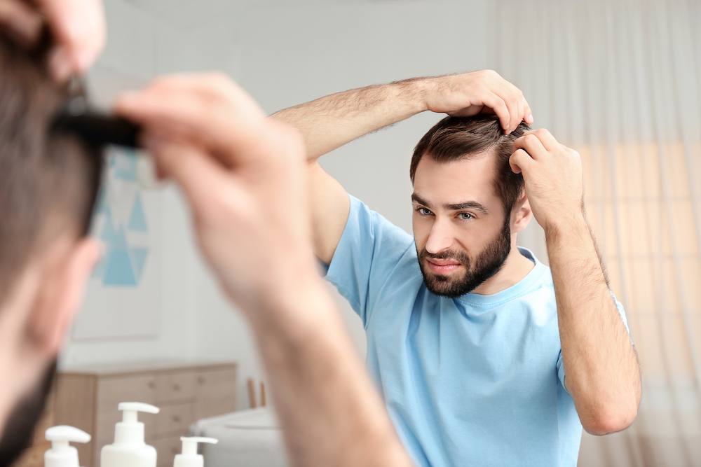 young man with hair loss problem front mirror indoors